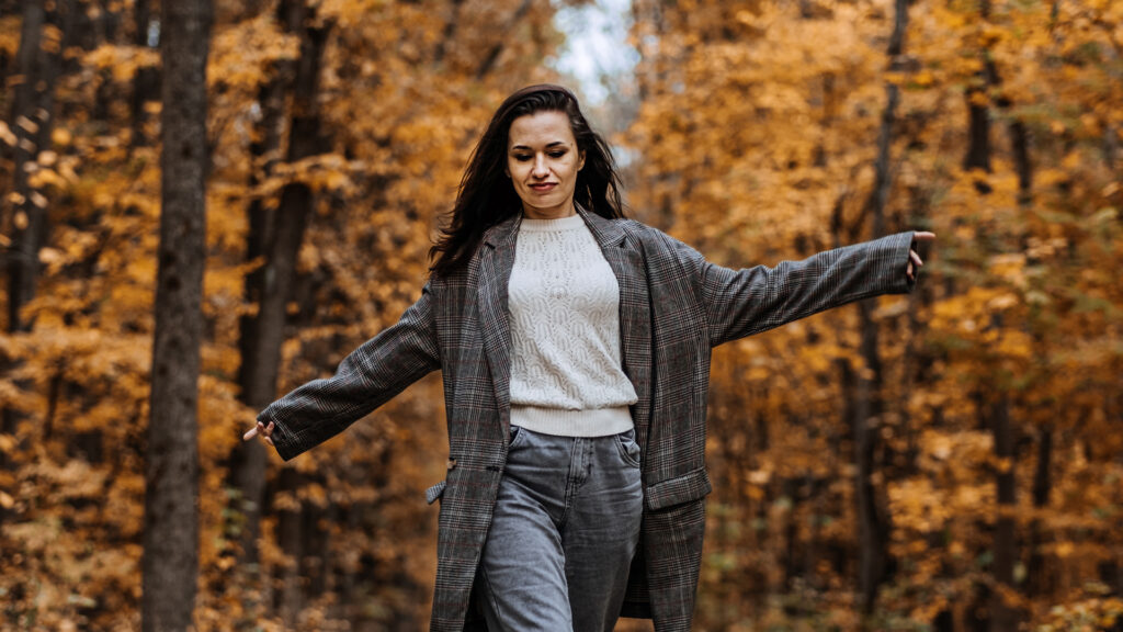 Iloinen nainen kävelee käsiään heilutellen syksyisessä maisemassa.