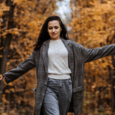 Iloinen nainen kävelee käsiään heilutellen syksyisessä maisemassa.