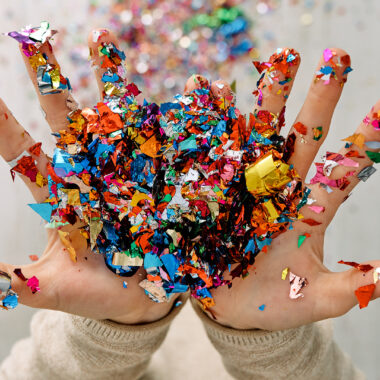 Kädet, jotka lähettävät ilmaan glittersilppua.