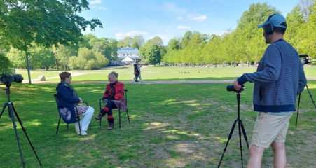 Videokuvaaja taltioi kahden tuoleilla istuvan naisen keskustelua kesäisessä puistossa.