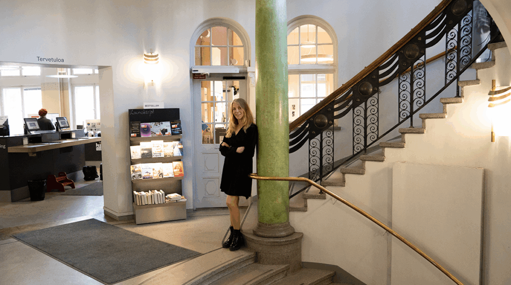 Riitta Taarasti seisoo kierreportaiden välitasanteella kirjaston sisäänkäynnin edessä.