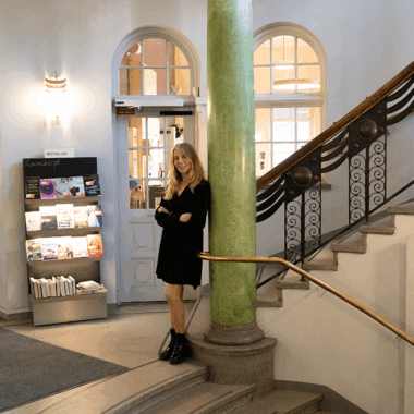 Riitta Taarasti seisoo kierreportaiden välitasanteella kirjaston sisäänkäynnin edessä.